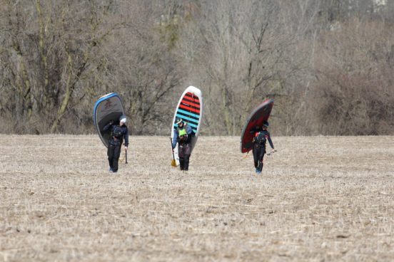 Three people carrying stand-up paddleboards on their backs.