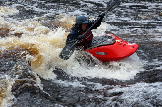 A man in a whitewater kayak about to surf in a whitewater hole.