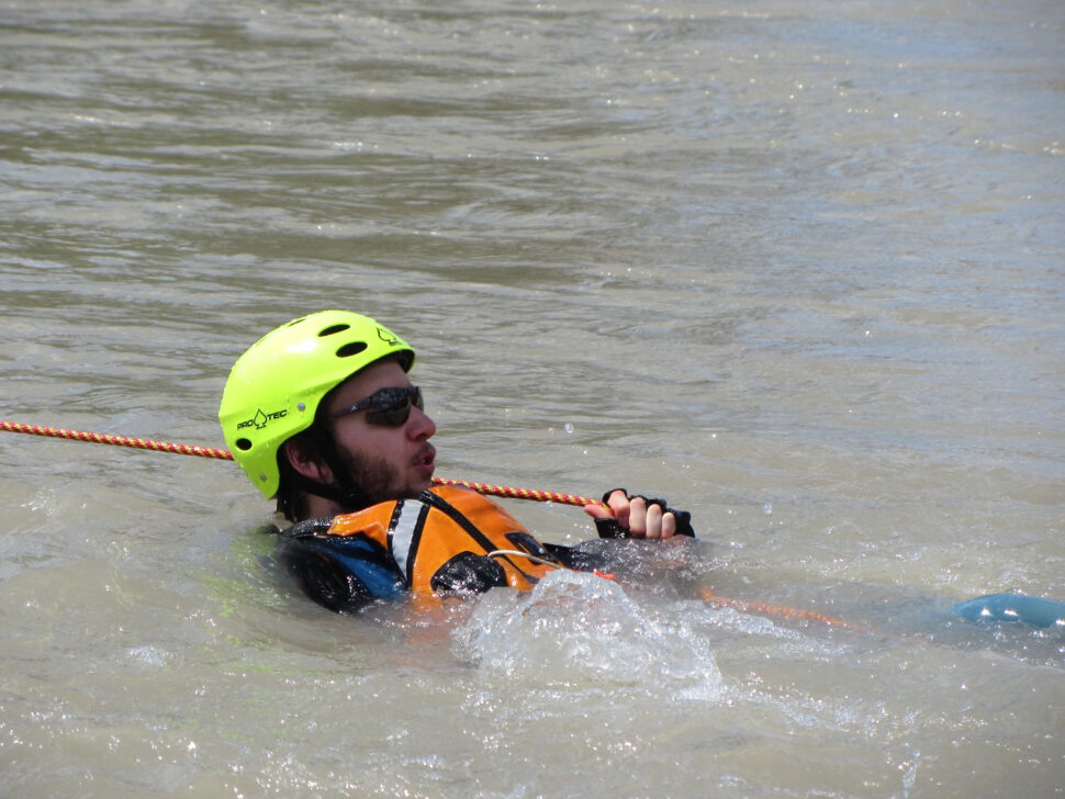 A swimmer in moving water during a river rescue course holding onto a rope.